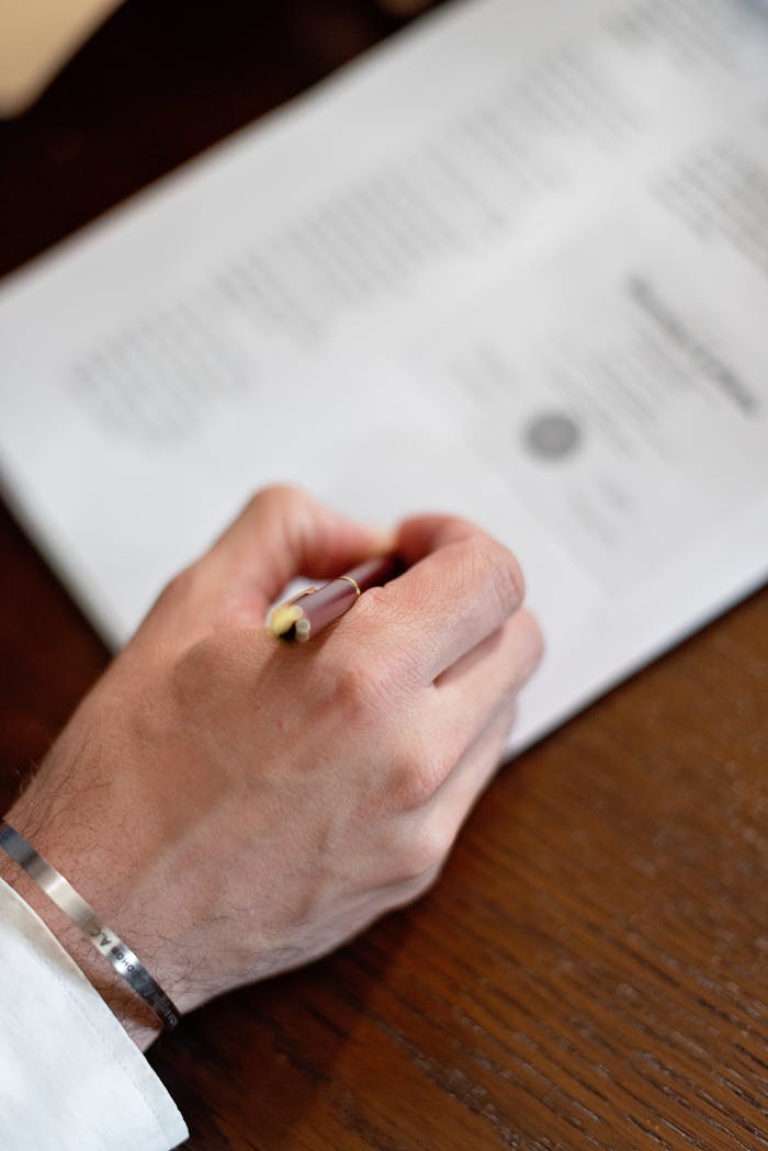 A close-up image of a hand holding a pen signing a formal document on a wooden table.